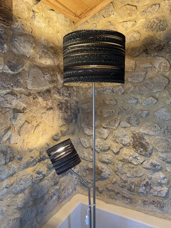 Lampe et applique en carton ajouré de l'Atelier La Pradella, sur un mur en pierre