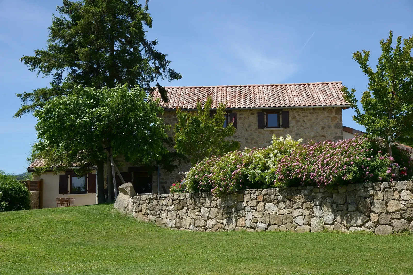 La maison en pierre de La Pradella et son mur fleuri d'hortensias, dans le jardin, en Ardèche Verte