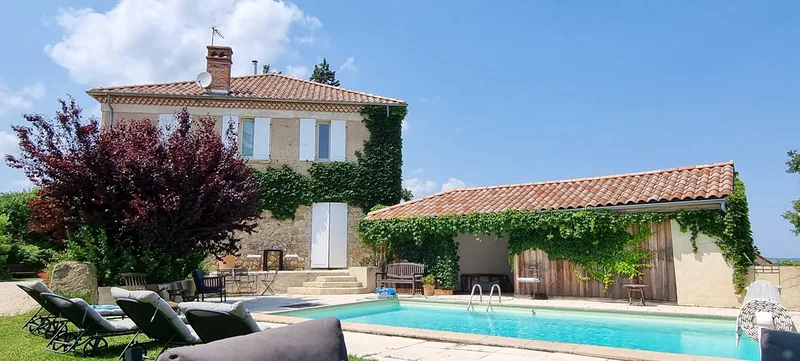 La façade de La Pradella couverte de verdure et la piscine bleue avec ses bains de soleil, en été