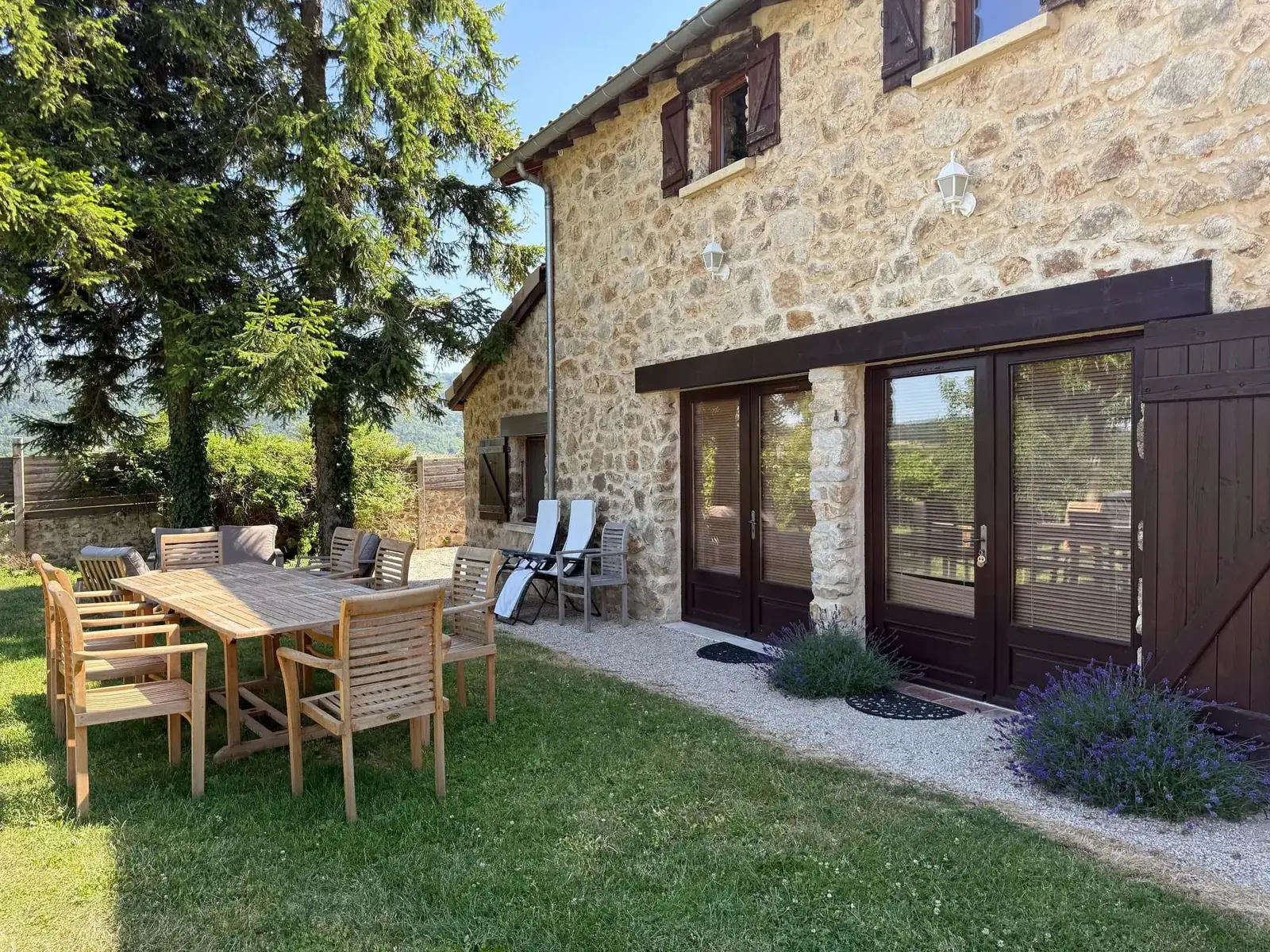 La grande table en teck sur la terrasse de La Pradella, devant la façade en pierre et ses lavandes, en Ardèche Verte