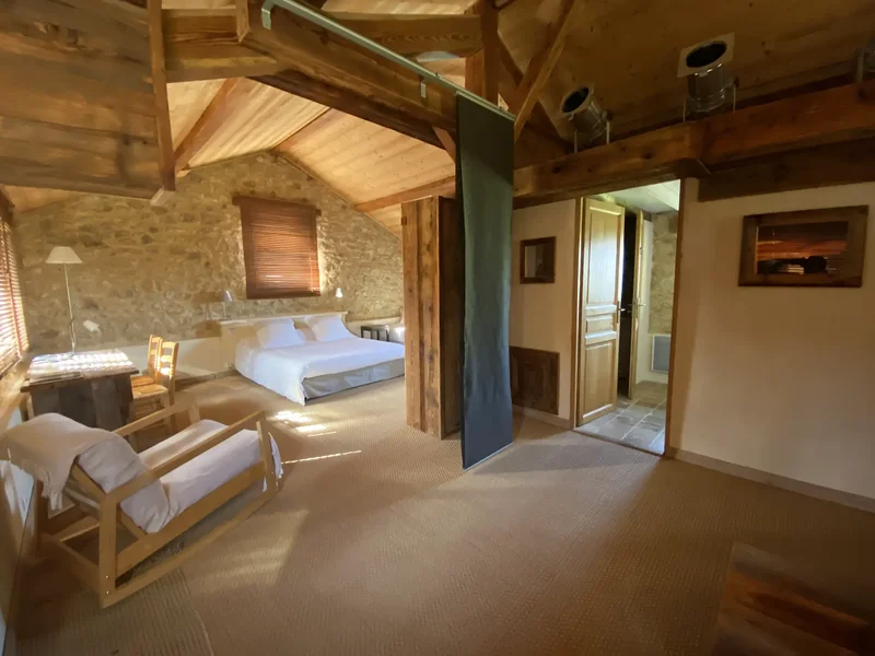 La Suite : la vaste chambre mansardée sous charpente, avec son lit, son coin salon et l'accès à la salle de bain