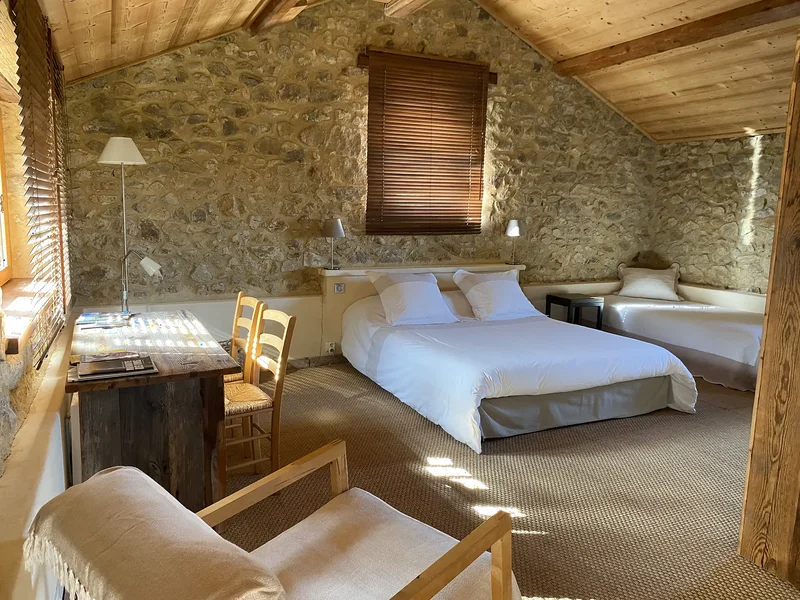 La Suite : le lit double face au mur en pierre, le bureau en bois ancien et le coin salon